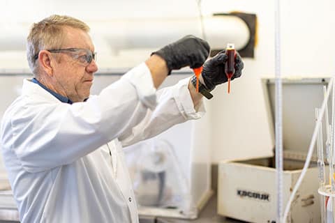 A person in a lab coat and gloves holding a tube with red liquid